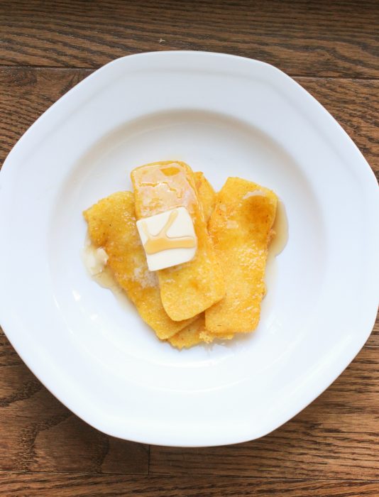 fried sliced cornmeal mush topped with butter on a white plate.