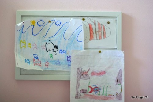 A white bulletin board with kid drawings hung on it.