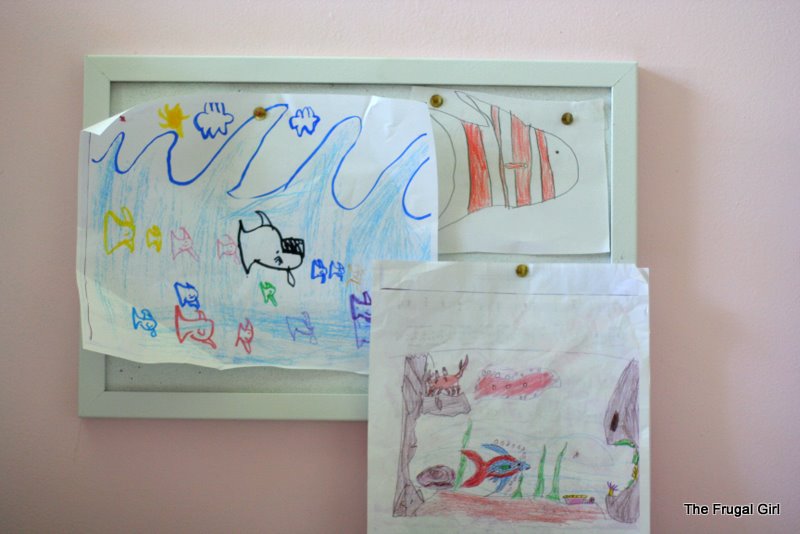 A white bulletin board with kid drawings hung on it.