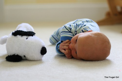 A baby lying on a floor next to a stuffed Snoopy dog.