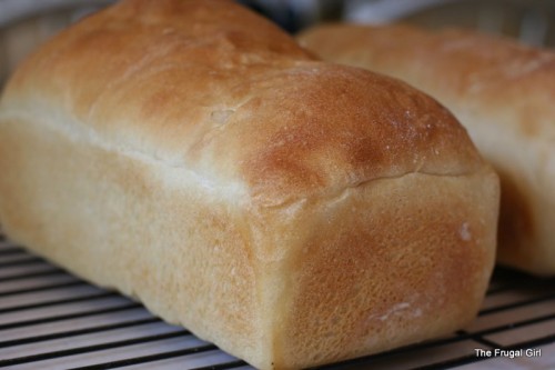 A baked loaf of white bread on a cooling rack.