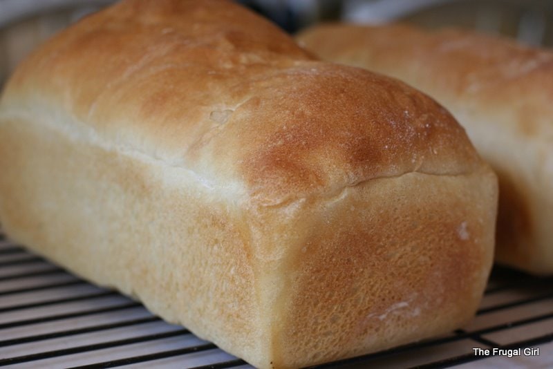 A baked loaf of white bread on a cooling rack.