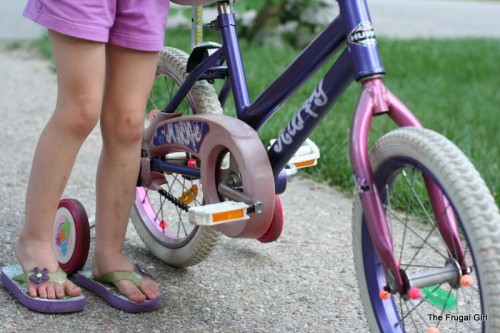 A little girl standing next to a purple bike.