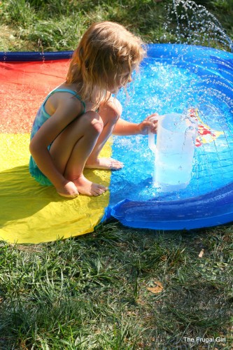 A little girl squatting next to a wading pool.