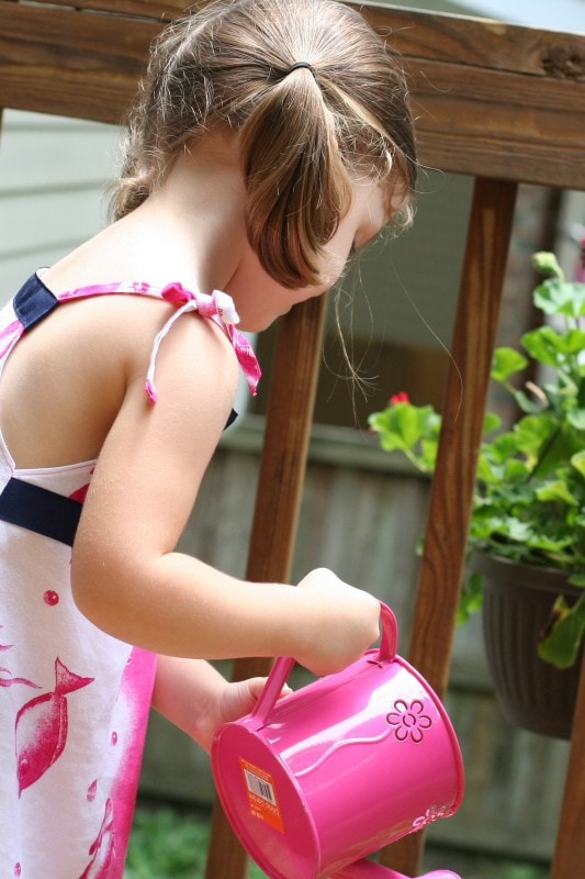 A little girl using a pink watering can.