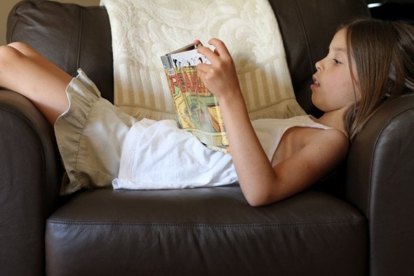 A girl lying down reading a Peanuts comic book.