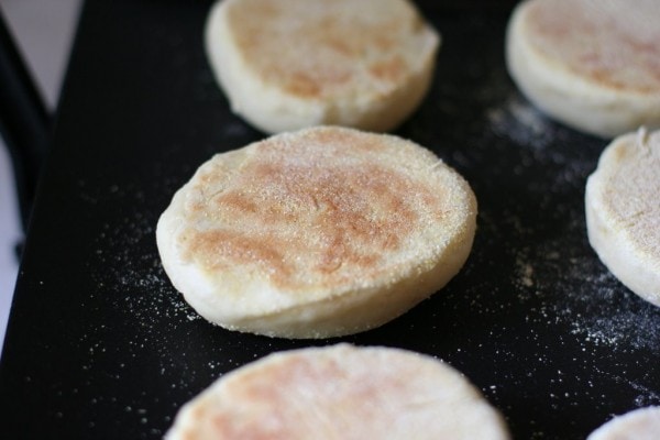 Partially-cooked English muffins on a griddle.