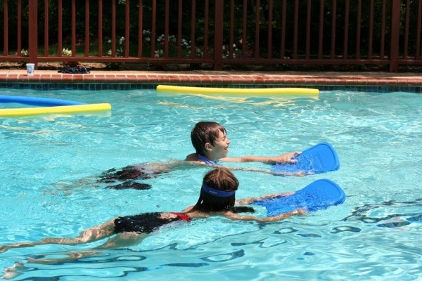 Two kids using kickboards in a pool.