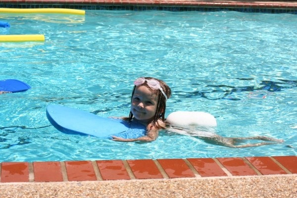 A preschool girl using a kickboard in a pool.