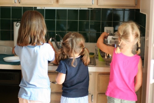 Three girls standing in front of a kitchen sink.