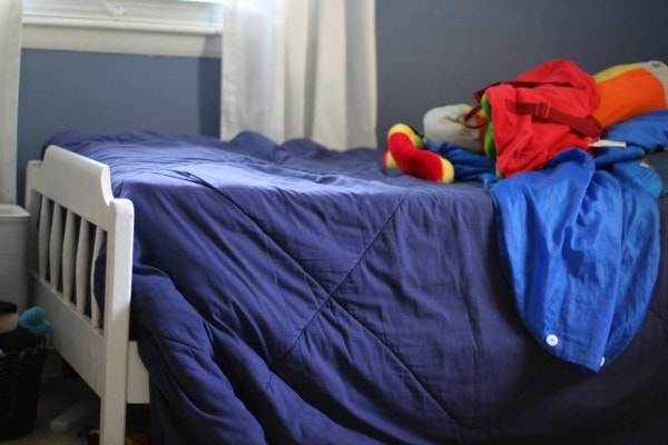 A white twin bed with a blue comforter.