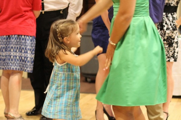 A little girl in a plaid dress dancing at a wedding.