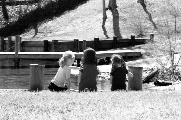 Three girls sitting on a pier by a river.