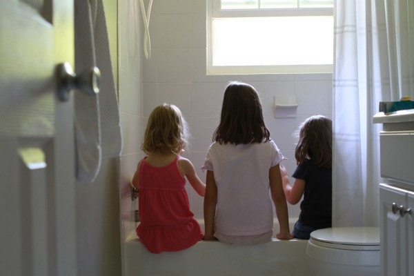 Three girls sitting on the edge of a bathtub, backs turned.