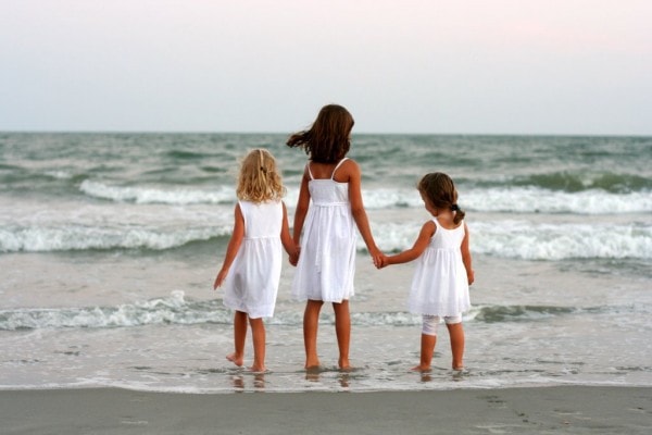 Three girls in white dresses on a beach.