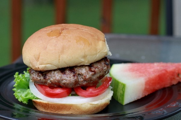 A hamburger and watermelon on a black plate.