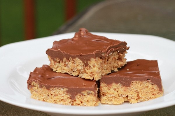 Chocolate frosted rice krispy treats stacked on a white plate.