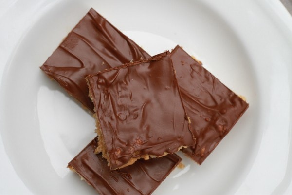 Square dessert bars with chocolate frosting, on a white plate.