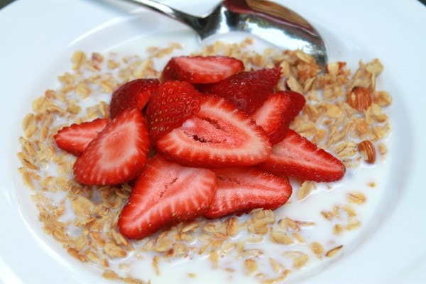 A bowl of granola, topped with strawberries and milk.
