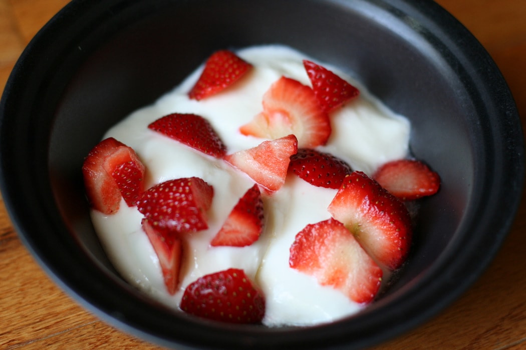 A black bowl of yogurt topped with strawberries.