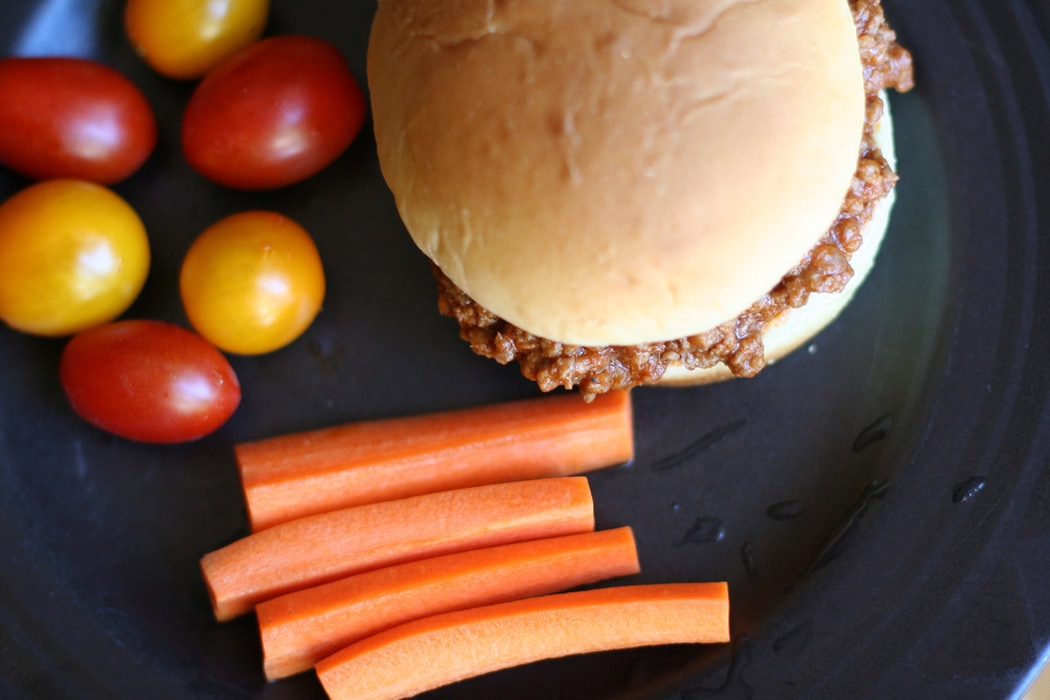 Sloppy Joe sandwich on a black plate, with carrots and tomatoes on the side.