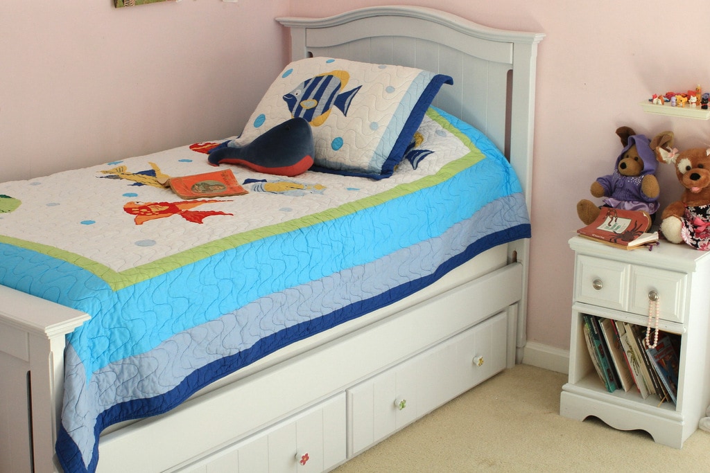 A white twin bed with a fish quilt on it.