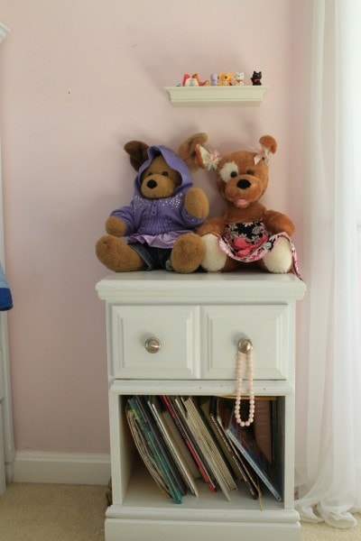 A white nightstand with two bears on top.