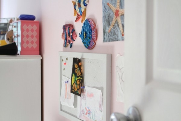 A white bulletin board hung on a pink wall.