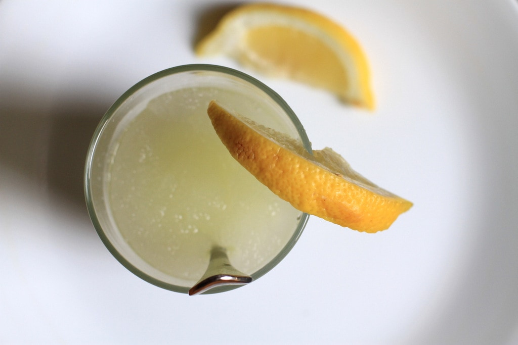 A lemonade slushie in a glass, topped with a lemon slice.