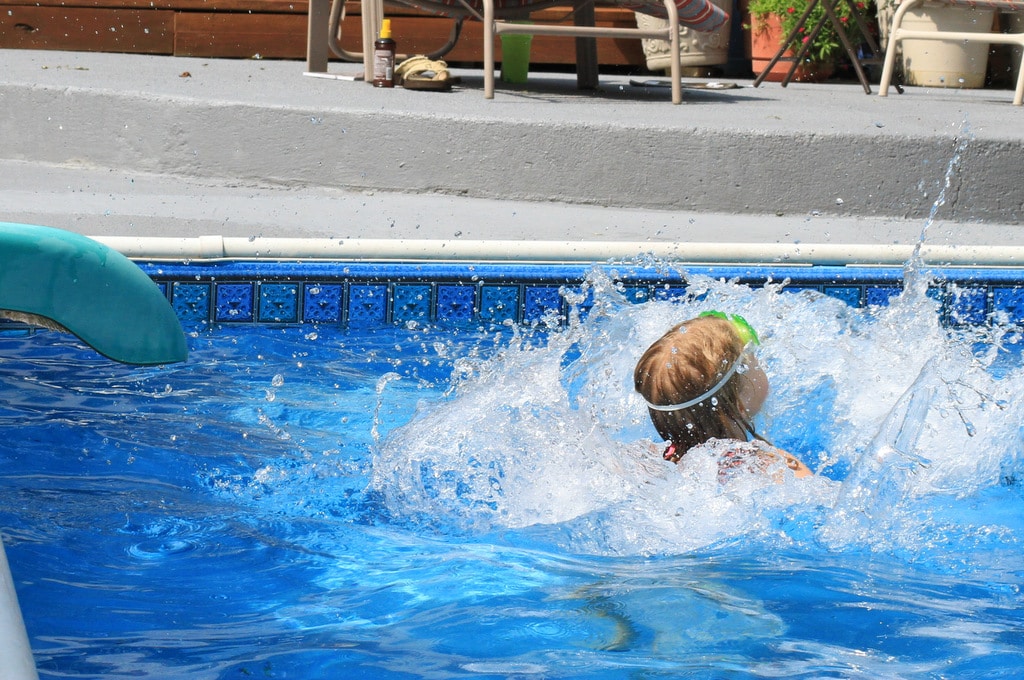 A little girl sliding into a pool from a waterslide.