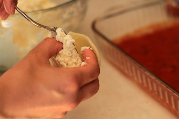 A pasta shell being filled with cheese.
