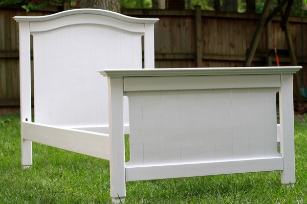 A white twin bed frame sitting on a green lawn.