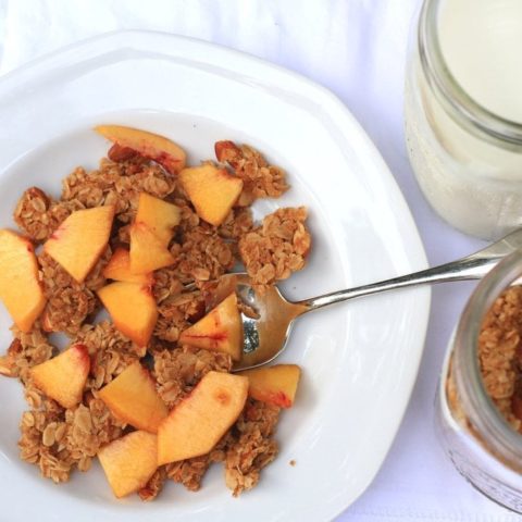 A bowl of granola, topped with sliced peaches, in a white bowl.