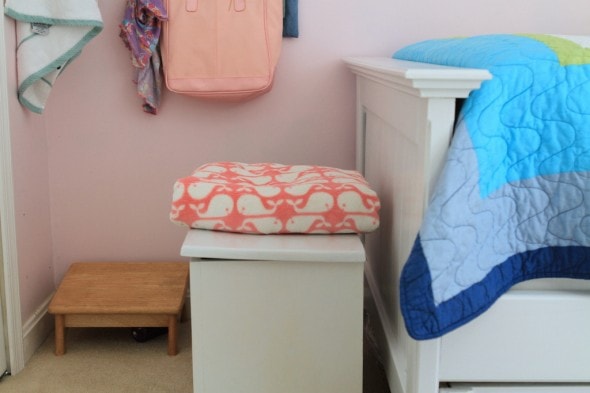 A white painted wood chest with a blanket on top.