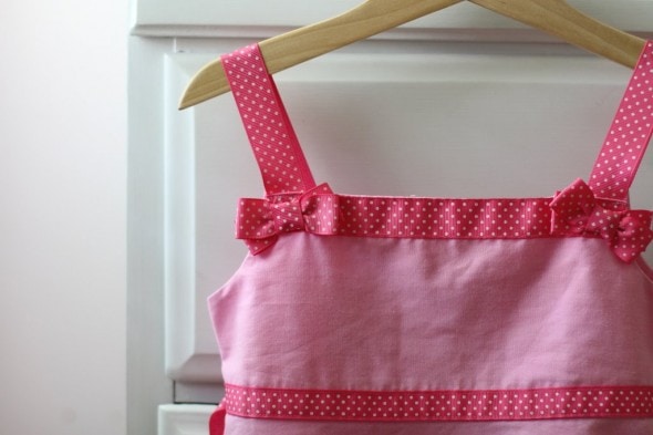 A girls pink dress with ribbon trim, on a hanger.