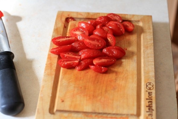 Sliced grape tomatoes on a wood cutting board.