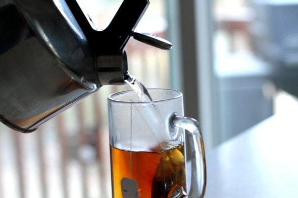 Water pouring from a kettle into a glass mug with a tea bag in it.