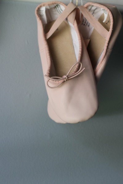 A pair of pink ballet shoes hanging from a hook.