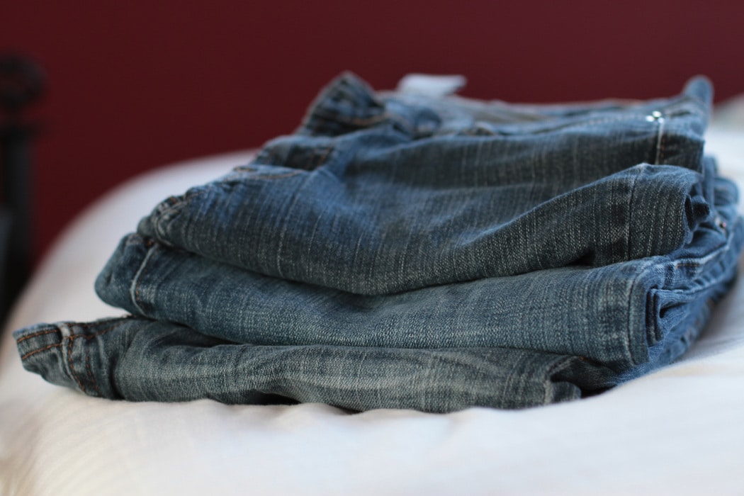 Three pairs of jeans, folded and stacked on a bed.