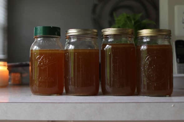 Four glass Mason jars of dark brown chicken broth.