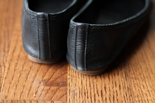 Two black ballet flats on a wood floor.