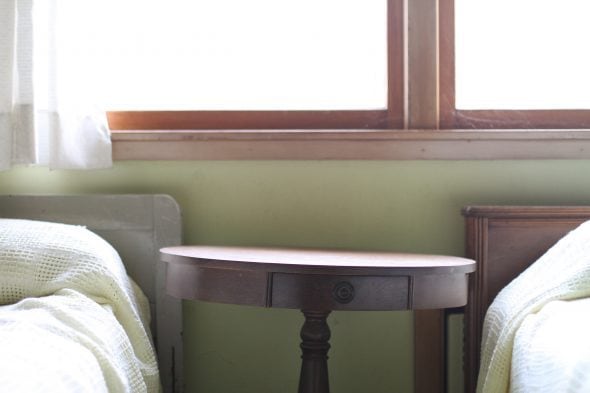 A round wooden night table against a green wall.