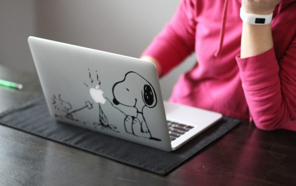 Kristen sitting at her Apple laptop, which has a Snoopy sticker on it.
