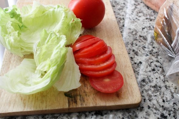 Lettuce and sliced tomatoes on a wooden cutting board.