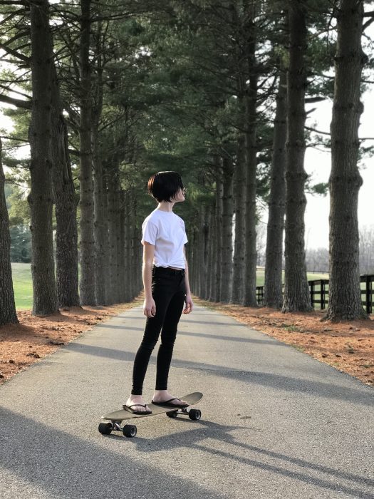 A teen girl with short black hair on a longboard.