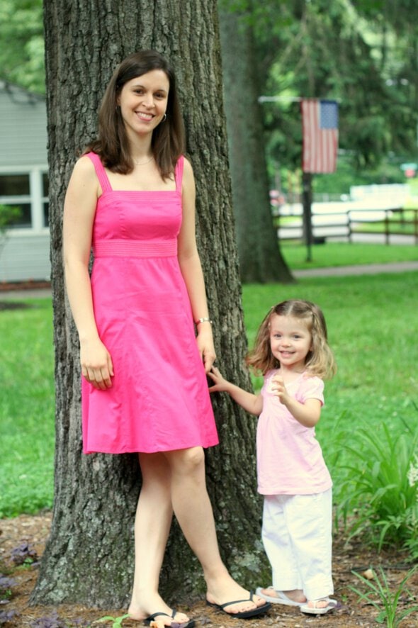 Kristen and toddler Zoe, standing by a tree.
