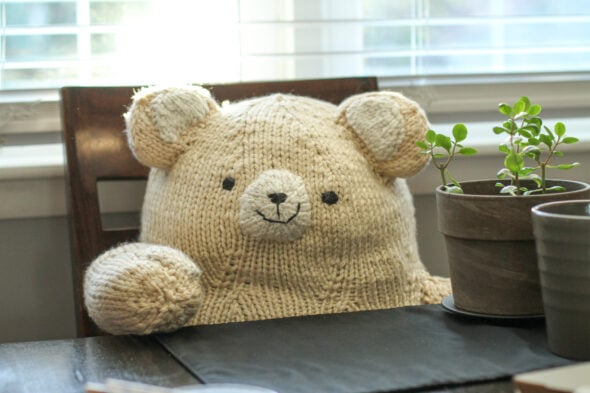 A large white knitted bear, sitting in a chair.