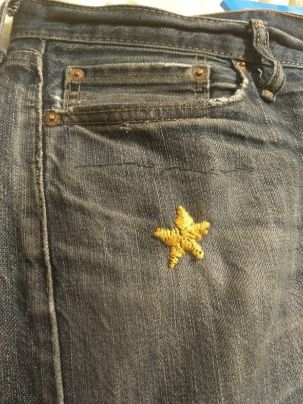 A hand-embroidered yellow star patch on jeans.