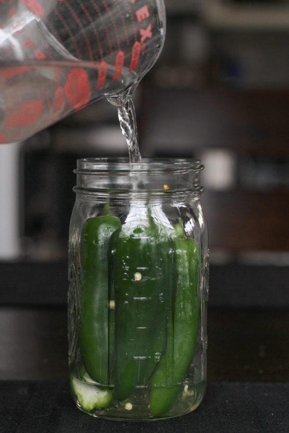 Brine being poured into a jar of jalapenos.