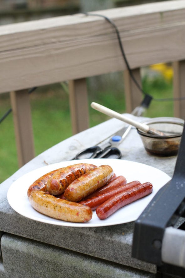 Grilled sausages and hot dogs on a plate next to a grill.